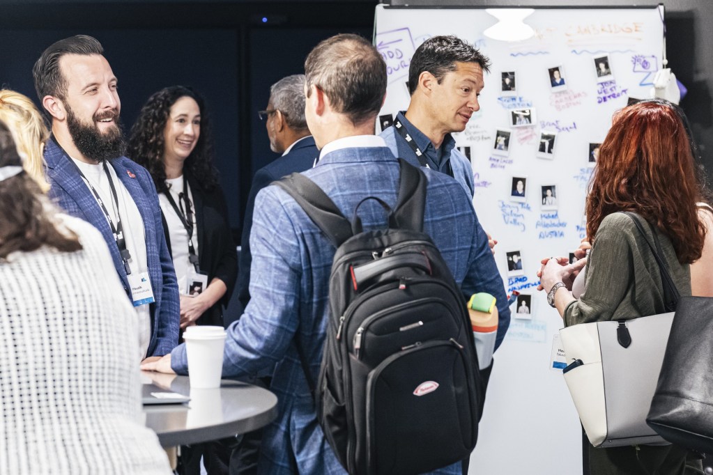 Impact participants network in front of the “wall of photos.”