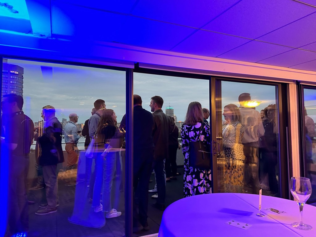Impact participants enjoy some drinks and networking on a balcony with a city view.
